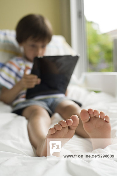 Junge entspannt auf dem Bett mit digitalem Tablett
