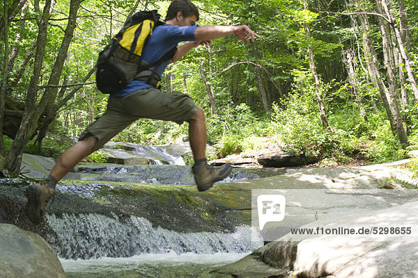 Mann springt über den Bach durch den Wald