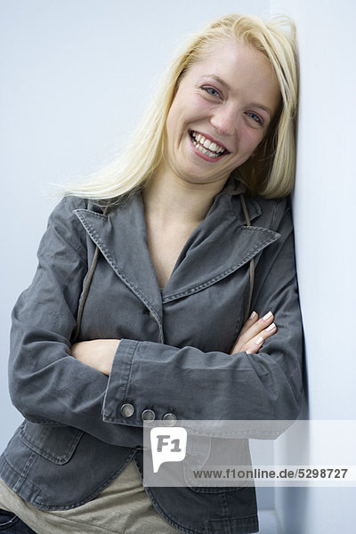 Young woman leaning against wall  smiling  portrait