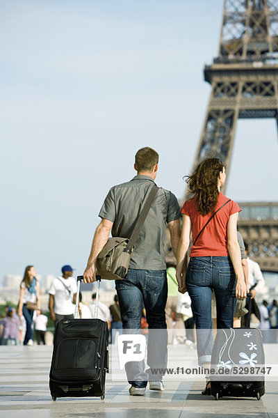 Couple walking with rolling luggage near Eiffel Tower  Paris  France