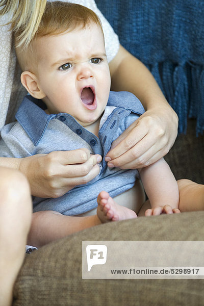 Baby yawning as mother dresses him