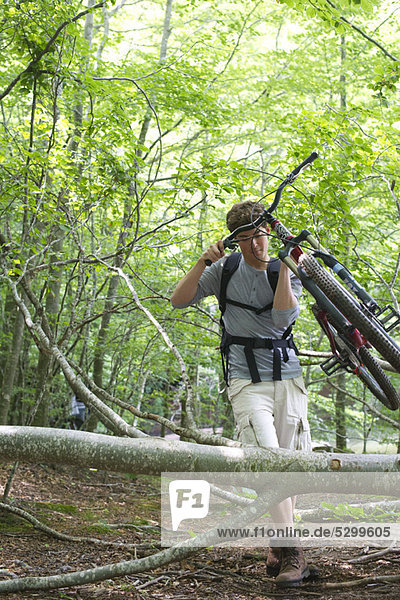 Man carrying mountain bike in woods with fallen tree trunks
