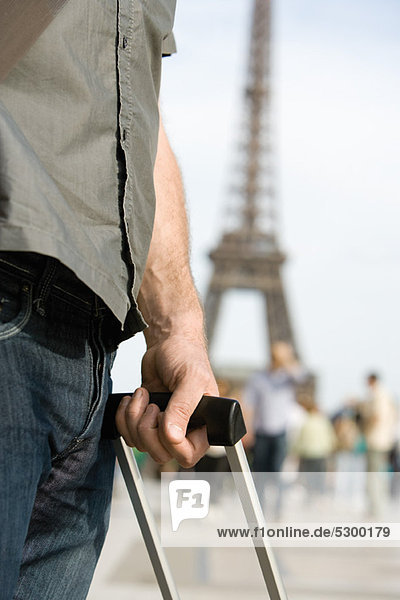 Man holding handle of rolling suitcase  Eiffel Tower visible in background  Paris  France