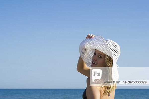 Frau mit Sonnenhut am Strand  Blick über die Schulter  Porträt