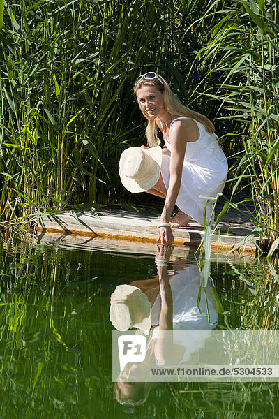 Frau hockt auf einem Holzsteg am Wasser