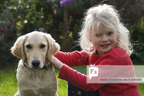 Blond girl sitting in a garden with a Golden Retriever  Upper Bavaria  Germany
