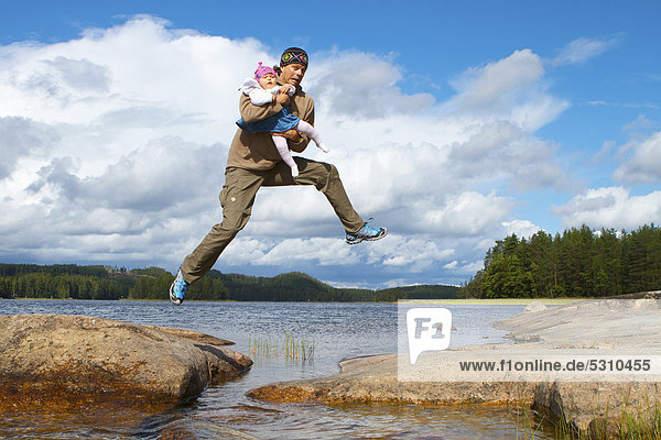 Man carrying a baby in his arms jumping across water  Mikkeli  Finland  Europe