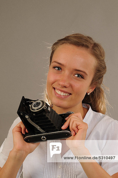 Lächelnde junge Frau mit einer alten Kamera  Balgenkamera
