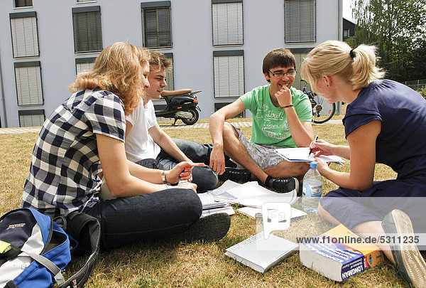 Studentengruppe sitzt auf Wiese vor Studentenwohnheim