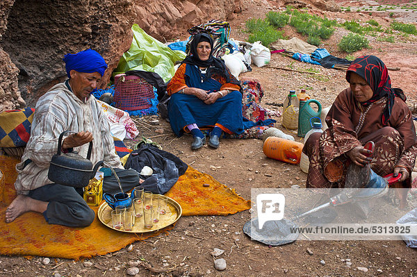 Höhlennomaden  Berber  ein Mann mit blauem Turban gießt Tee ein  eine Frau bringt mit einem Blasebalg Holzkohle für die Zubereitung von Tee zum Glühen  Dades-Tal  Hoher Atlas  Südmarokko  Marokko  Afrika
