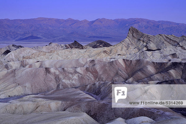 Blick von Zabriskie Point auf durch Mineralien verfärbtes erodiertes Gestein des Manly Beacon  dahinter Panamint Range  Morgendämmerung  Death Valley Nationalpark  Mojave-Wüste  Kalifornien  Vereinigte Staaten von Amerika  USA