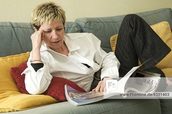 Woman lying on a sofa  reading a magazine