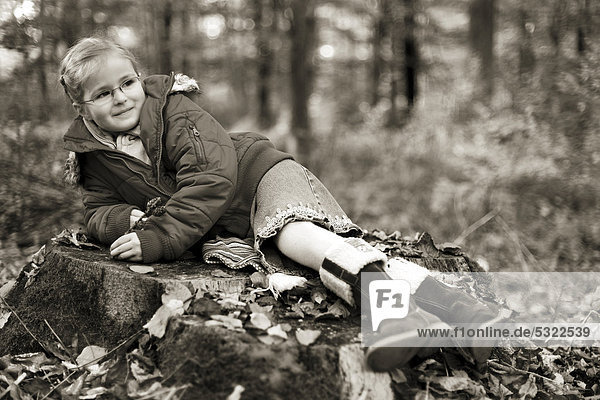 Fünfjähriges Mädchen liegt auf Baumstumpf im Wald  in Sepia