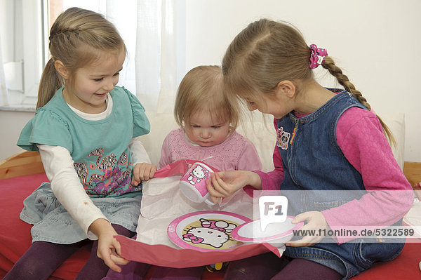 Zwei Schwestern  5 und 6 Jahre  helfen der kleinen Schwester  2 Jahre  beim Auspacken eines Geschenkes