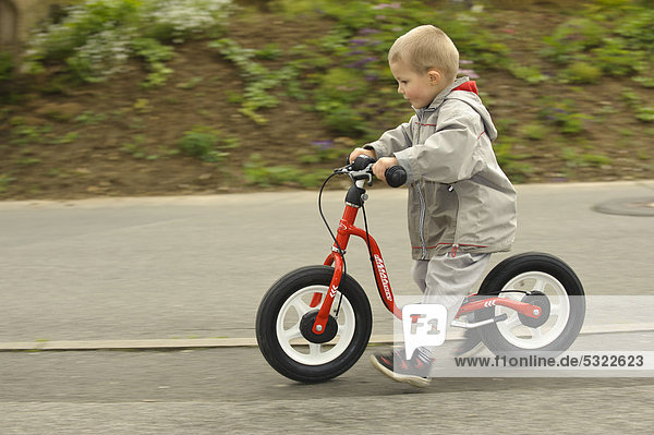 Junge  4 Jahre  fährt mit Laufrad auf dem Gehweg