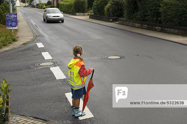 7-year-old girl with yellow safety vest for school children waiting to cross the wet main street  Assamstadt  Baden-Wuerttemberg  Germany  Europe