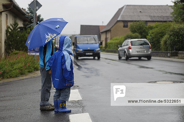 Zwei Kinder  4 und 8 Jahre  wollen im Regen die Straße überqueren  zwei Autos  Assamstadt  Baden-Württemberg  Deutschland  Europa