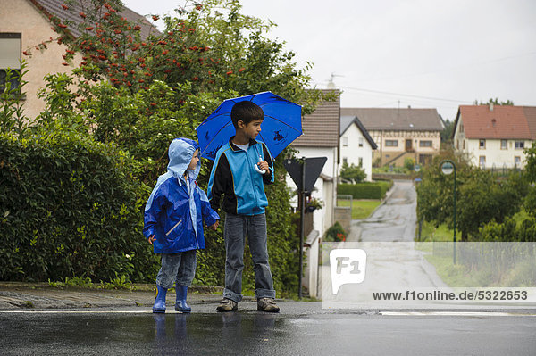 Zwei Kinder  4 und 8 Jahre  überqueren im Regen die Straße  Assamstadt  Baden-Württemberg  Deutschland  Europa