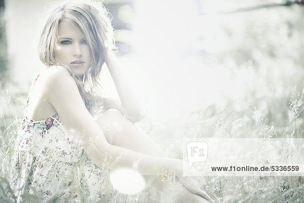 Junge Frau im Sommerkleid sitzt im hohen Gras