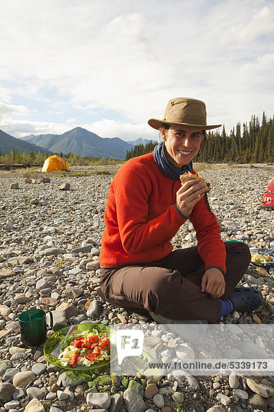Junge Frau genießt einen Hamburger  Zelt hinten  Camping  Wind River  Yukon Territory  Kanada