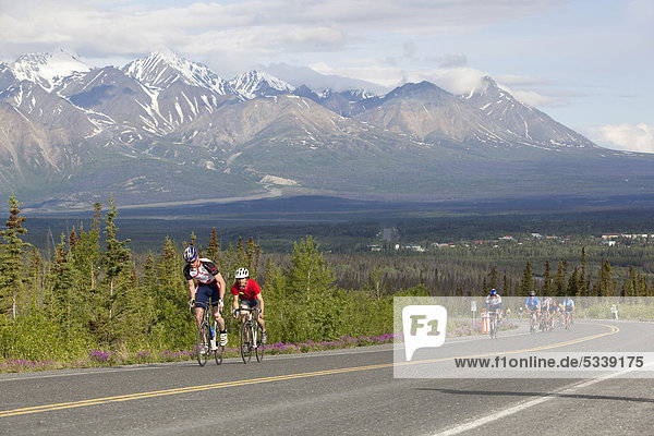 Cyclists racing in front of St. Elias mountain  at the Kluane Chilkat International Bike Relay  bicycle race from Haines Junction Yukon Territory  Canada  to Haines  Alaska  USA