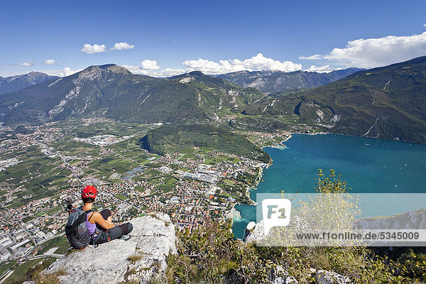 Climber sitting on the Via dell' Amicizia fixed rope route  Lake Garda  the village of Riva below  province of Trento  Italy  Europe