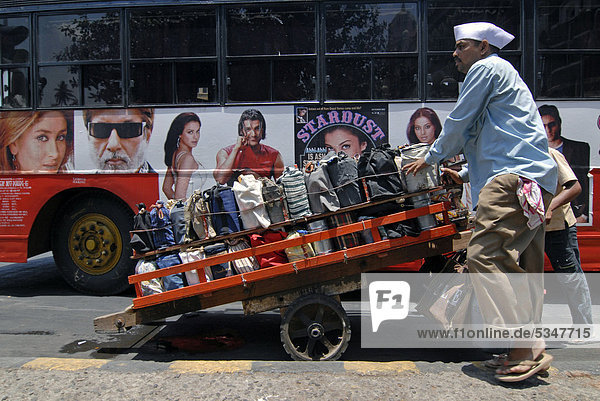 Dabba wallah or food deliverer with a pallet of Dabbas or food containers  near Churchgate station in front of a bus with pictures of Bollywood stars  Mumbai  India  Asia