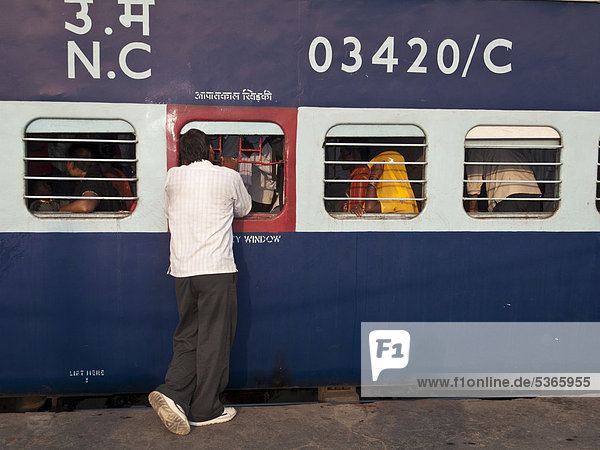 Mann redet mit Zugpassagieren bevor sich der Zug in Bewegung setzt  New Delhi Railway Station  New Delhi  Neu-Delhi  Indien  Asien