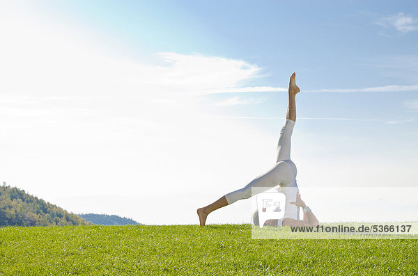 Junge Frau praktiziert Hatha-Yoga im Freien  zeigt die Stellung sarvangasana  ardha halsasana  Schulterstand  halber Pflug  Nove Mesto  Okres Teplice  Tschechische Republik  Europa