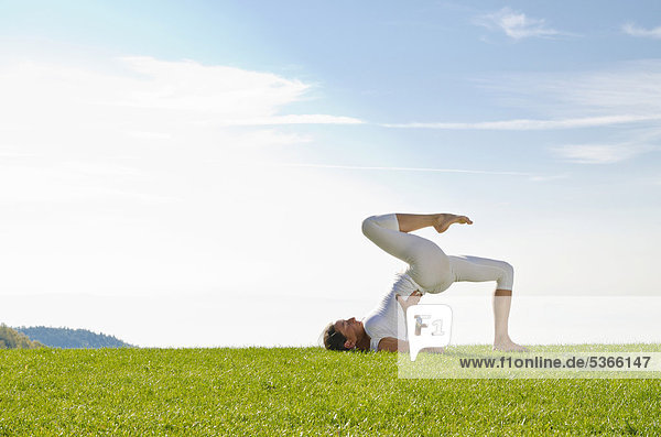 Junge Frau praktiziert Hatha-Yoga im Freien  zeigt die Stellung setu bandhasana  kandharasana  Brücke  Nove Mesto  Okres Teplice  Tschechische Republik  Europa