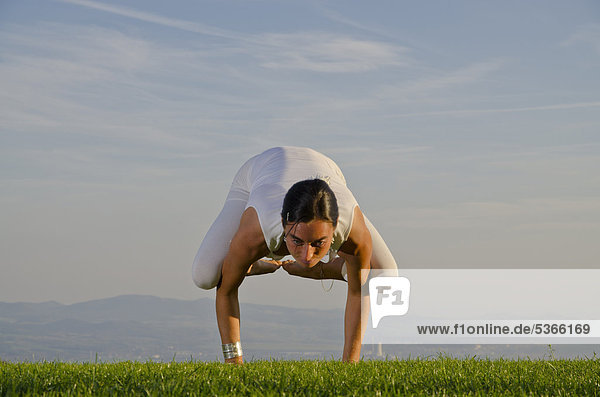Junge Frau praktiziert Hatha-Yoga im Freien  zeigt die Stellung kakasana  bakasana  Krähe  Kranich  Nove Mesto  Okres Teplice  Tschechische Republik  Europa