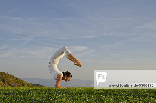Junge Frau praktiziert Hatha-Yoga im Freien  zeigt die Stellung vrischikasana  Skorpion  Nove Mesto  Okres Teplice  Tschechische Republik  Europa