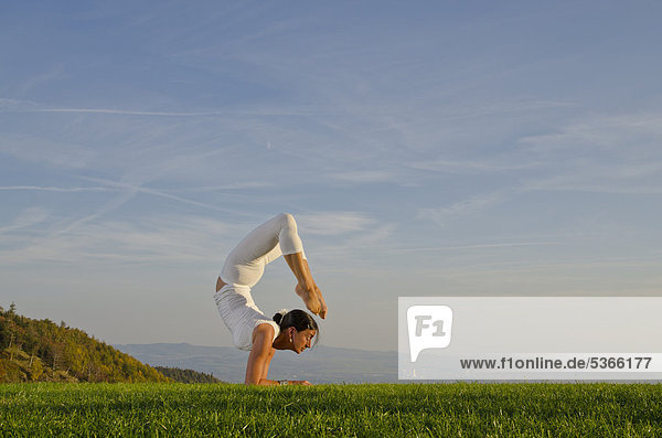 Junge Frau praktiziert Hatha-Yoga im Freien  zeigt die Stellung vrischikasana  Skorpion  Nove Mesto  Okres Teplice  Tschechische Republik  Europa