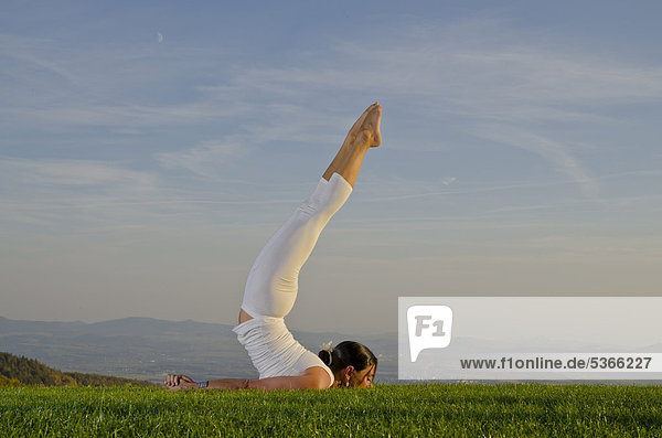 Junge Frau praktiziert Hatha-Yoga im Freien  zeigt die Stellung shalabhasana  Heuschrecke  Nove Mesto  Okres Teplice  Tschechische Republik  Europa