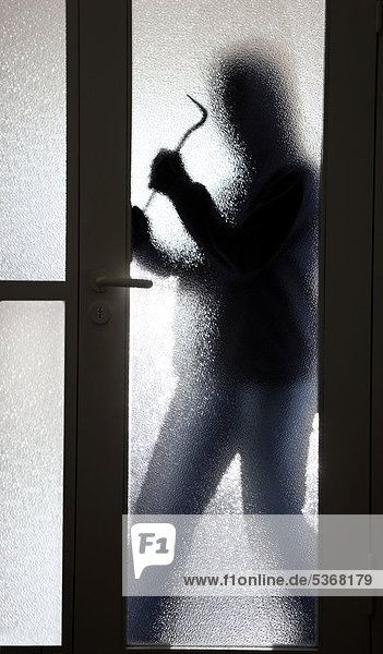 Einbruch  Wohnungseinbruch  Einbrecher tagsüber im Treppenhaus eines Mehrfamilienhauses bricht eine Glastür auf
