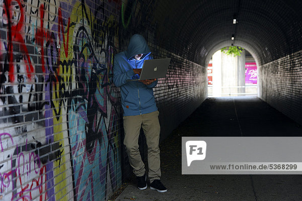 Man surfing on a laptop computer in a pedestrian tunnel  symbolic image for computer hacking  computer crime  cybercrime  data theft