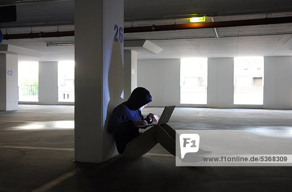 Mann surft mit Laptop in einem leeren Parkhaus  Symbolbild Computerhacker  Computerkriminalität  Internetkriminalität  Datenklau