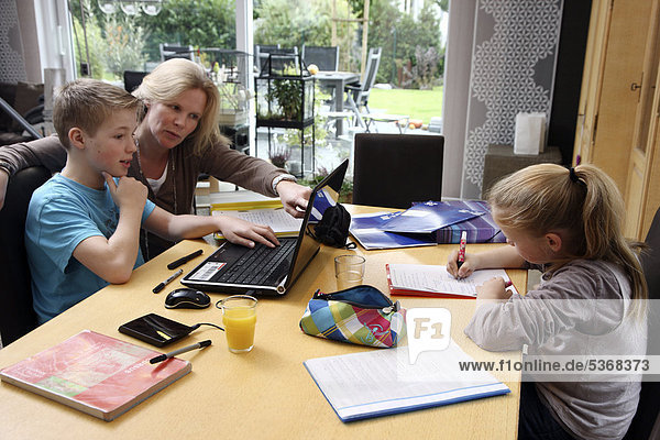 Geschwister machen im Wohnzimmer gemeinsam Hausaufgaben  mit Hilfe der Mutter