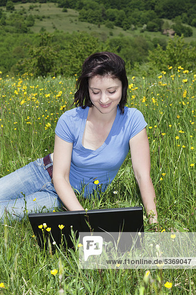 Young woman with a laptop in a meadow