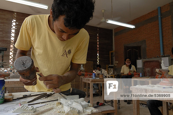 Junger kambodschanischer Kunsthandwerker bei der kunsthandwerklichen Verarbeitung von Stein mit Holzhammer und Meißel zur Herstellung einer traditionellen Apsarafigur  Apsaratänzerin  Artisans d'Angkor  Angkor  Siem Reap  Kambodscha  Indochina  Südostasien  Asien