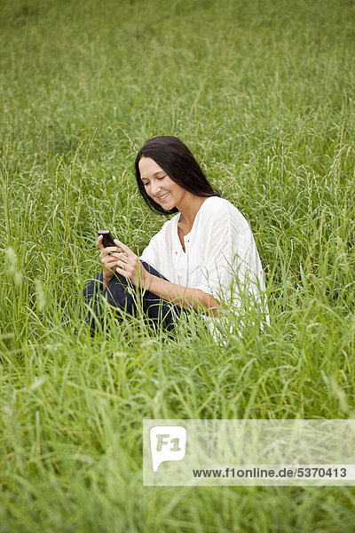 Young woman sitting in the long grass  using a mobile phone