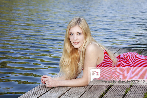 Junge Frau liegt entspannt auf einem Steg am Wasser