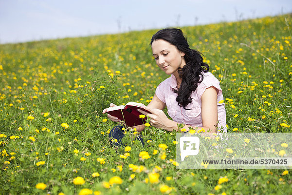 Junge Frau sitzt auf einer Wiese  liest ein Buch