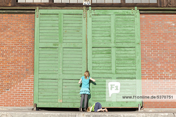 Kinder schauen neugierig durch das Tor einer Lagerhalle  Hafen  Hamburg Wilhelmsburg  Deutschland  Europa