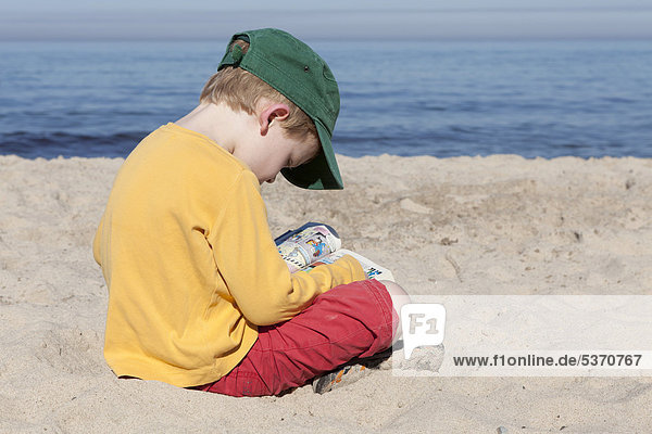 Kleiner Junge liest am Strand  Kühlungsborn-West  Mecklenburg-Vorpommern  Deutschland  Europa