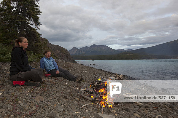 Zwei junge Frauen sitzen an einem Lagerfeuer  Ufer des Atlin Lake Sees  British Columbia  Kanada  Amerika