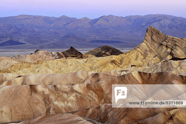 Blick von Zabriskie  auch Zabriske Point  auf durch Mineralien verfärbtes erodiertes Gestein des Manly Beacon  dahinter Panamint Range  Morgendämmerung  Death Valley Nationalpark  Mojave-Wüste  Kalifornien  Vereinigte Staaten von Amerika  USA