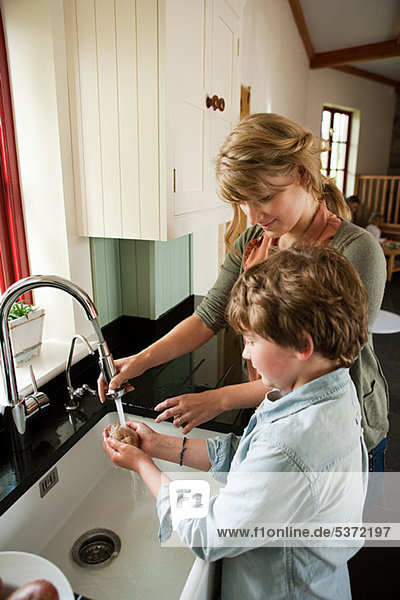 Mother and son washing potatoes in kitchen sink
