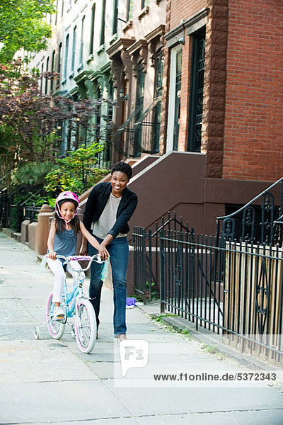 Lernen zu fahren Fahrrad auf Bürgersteig mit Mutter Tochter