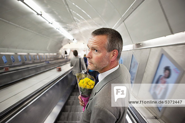 Mann auf U-Bahn Rolltreppe mit Blumen
